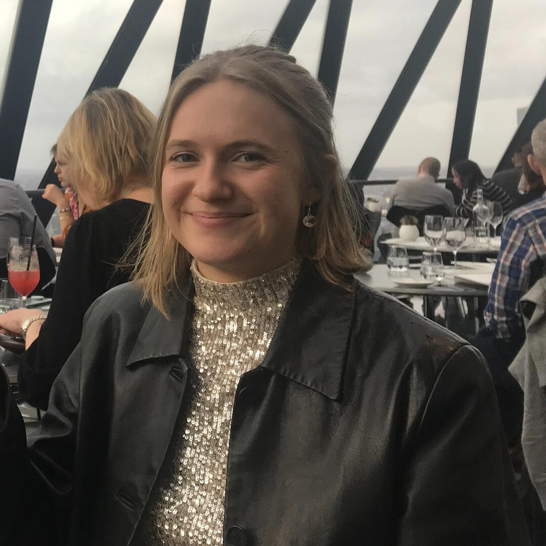Katarina, a white woman with short fair hair, is sitting at a restaurant table. She wears a black jacket over a sparkly silver top.
